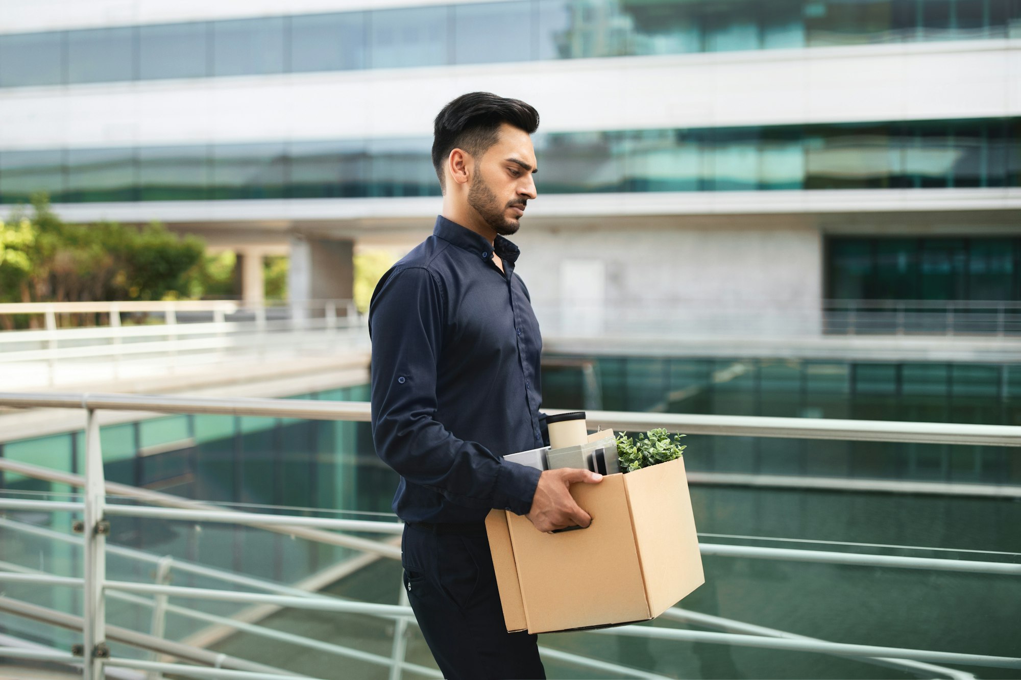 Young Arabian man with carton box leaving modern office building